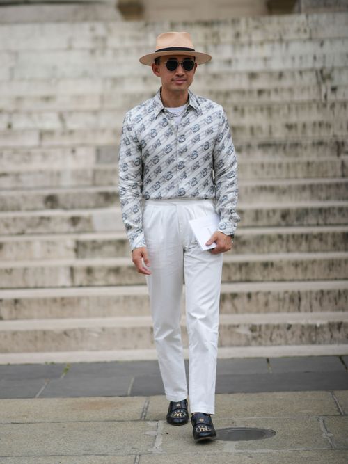 Norman Tan trägt ein gemustertes Hemd mit weißer Hose, Hut und Sonnenbrille auf der Paris Fashion Week.