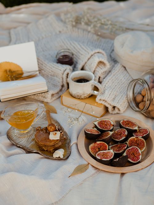 Auf einer weißem Decke ist ein Teller mit geschnittenen Feigen und ein gelbes Buch.