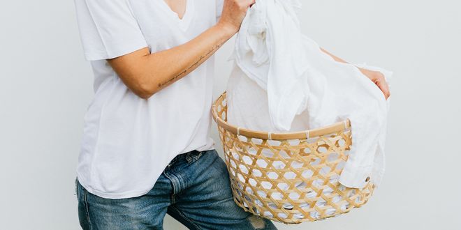 Close-up von einer Frau in Jeans mit weißem T-Shirt die einen Wäschekorb mit weißer Wäsche hält.