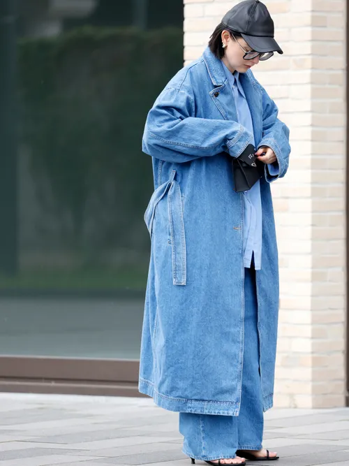 Maria Barteczko, wearing a blue denim oversized trenchcoat by Teurn, a blue button down shirt by Teurn, blue denim wide leg jeans by Teurn, a black leather baseball cap by Arket, black kitten heel strap sandals by Teurn, a black mini Kelly bag by Hermes, silver hoops earrings by H&M and black oversized Aviator glasses by Victoria Beckham, during a streetstyle shooting.