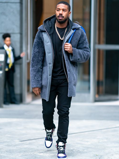 Michael B. Jordan in einem schwarzen Look und einem grauen Shearling Mantel.
