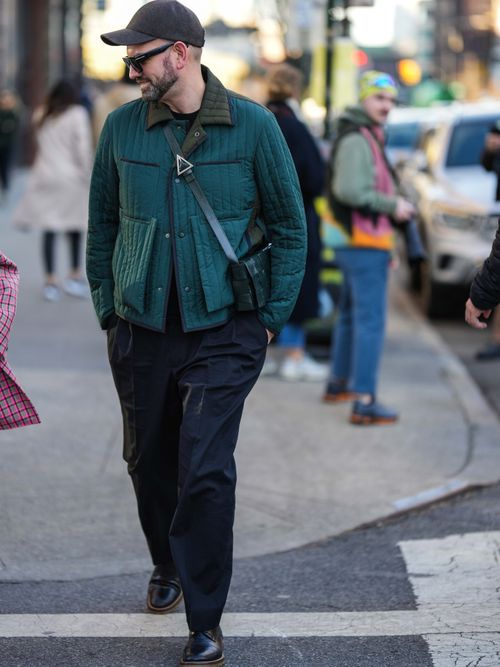 Ein Gast auf der New York Fashion Week trägt eine dunkelgrüne Jacke, mit Sonnenbrillen, schwarze Hose und schwarzen Schuhen.
