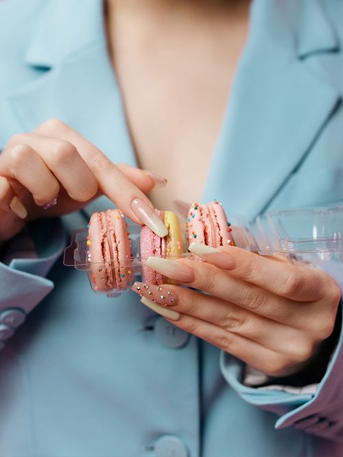 Close up von einer Frau in einem hellblauen Blazer mit Macarons in der Hand und Babyboomer Nails.