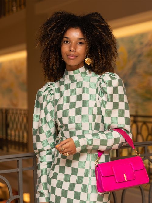 Frau mit einem grün-weißen Kleid mit Puffärmeln im Schachbrett-Muster und eine pinken Handtasche.