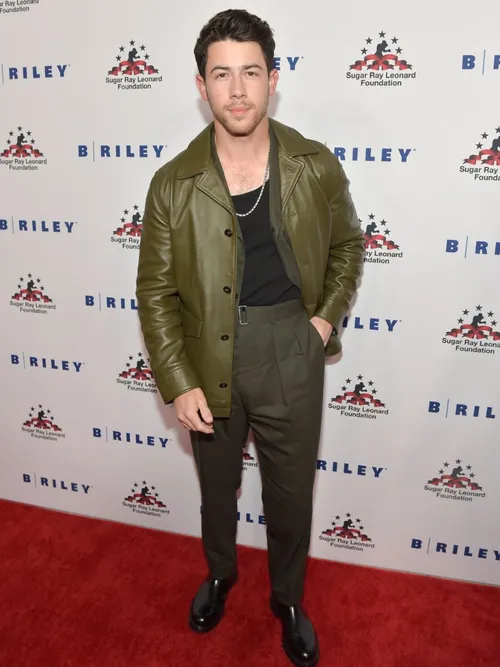 Nick Jonas am Red Carpet und trägt eine grüne Lederjacke mit einer High Waist Hose und schwarzem T-Shirt in Los Angeles.