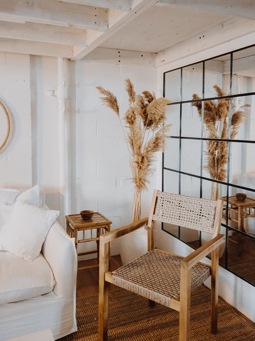 Rattanstuhl und weißes Sofa vor einer Spiegelwand und einem großen Strauß Pampasgras.