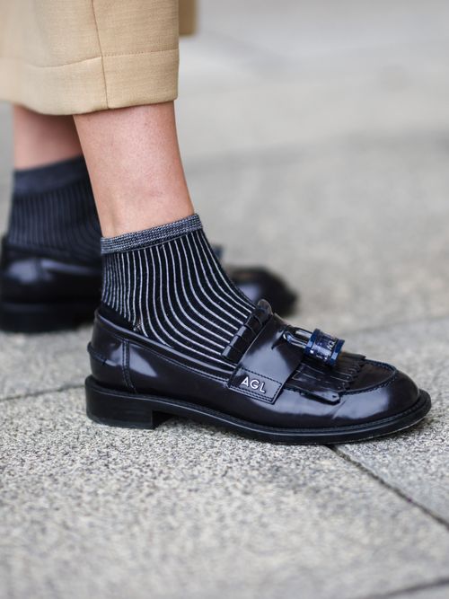 Close-up von Natalia Verza, die einen dunkelblauen Tassel Loafer mit gestreiften Socken trägt.
