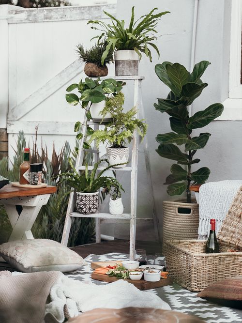 Balkon mit einer weißen Leiter als Pflanzenhalter mit Deko aus Rattan.