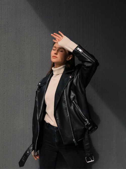 Street Style Look von einer Frau, die eine schwarze Lederjacke mit schwarzer Hose und beigem Rollkragen trägt.