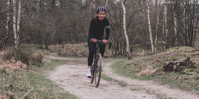 Radfahrerin mit Helm und schwarzem Sportoutfit radelt durch einen Park.
