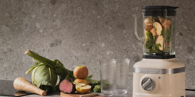 Ein Kichten Aid Standmixer der neben Gemüse und zwei Gläsern steht.