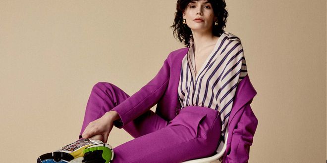 Frau in lila Hosenanzug mit gestreifter Bluse uns Sneakers
