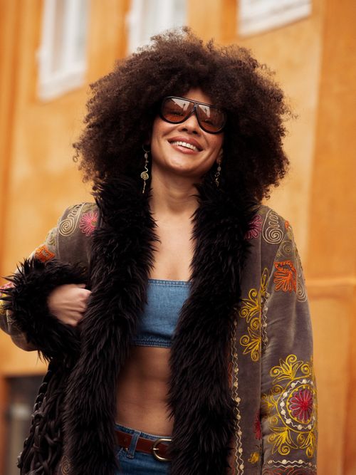 Julia Dalia wears white blue jeans, a blue bikini top, and a long brown, red, and black coat outside Lovechiled 1979 during the Copenhagen Fashion Week AW24 on January 30, 2024 in Copenhagen, Denmark.