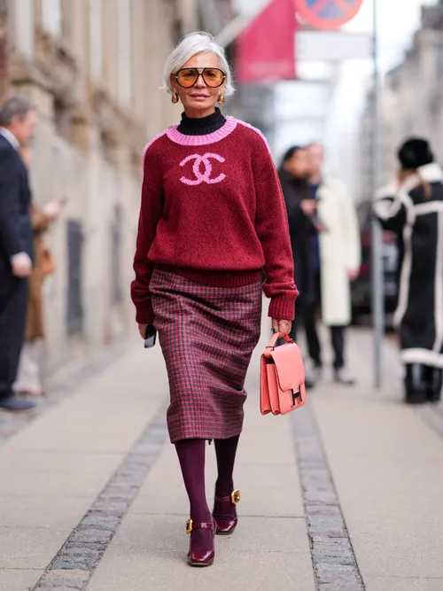Grece Ghanem wears sunglasses, golden earrings, a black turtleneck pullover , a pink and red Chanel pullover, a red midi checkered / checked pattern printed skirt , burgundy leggings, matching leather shoes, a Hermes pink bag, outside The Garment, during the Copenhagen Fashion Week AW24 on January 31, 2024 in Copenhagen, Denmark.