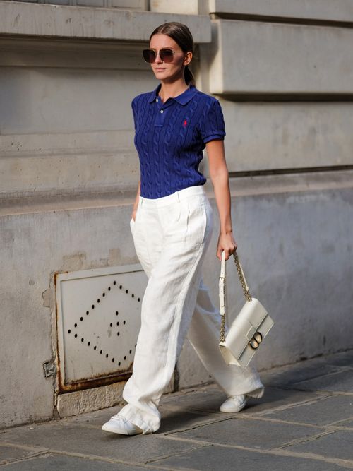 Diane Batoukina trägt ein dunkelblaues Poloshirt, weiße Leinenhose, weiße Ledertasche und Leinen-Sneaker in Paris.