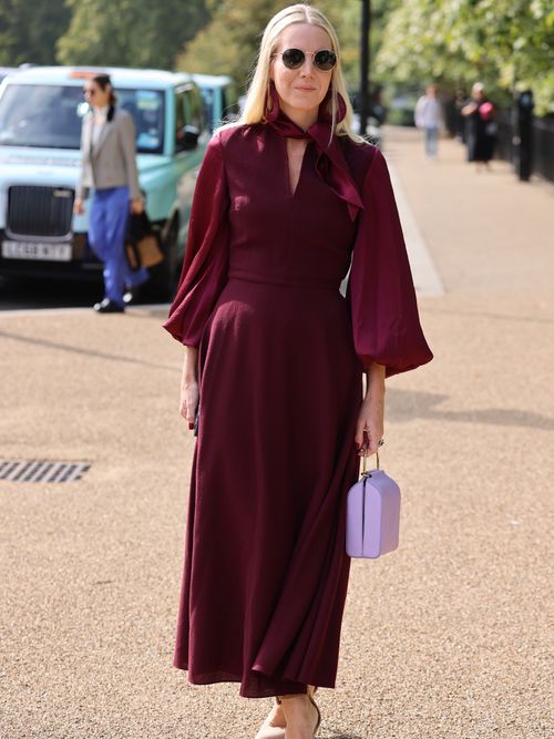 Street Style Look von der London Fashion Week, wo ein Gast ein burgunderfarbenes Kleid mit einer fliederfarbenen Tasche und nude Pumps trägt.