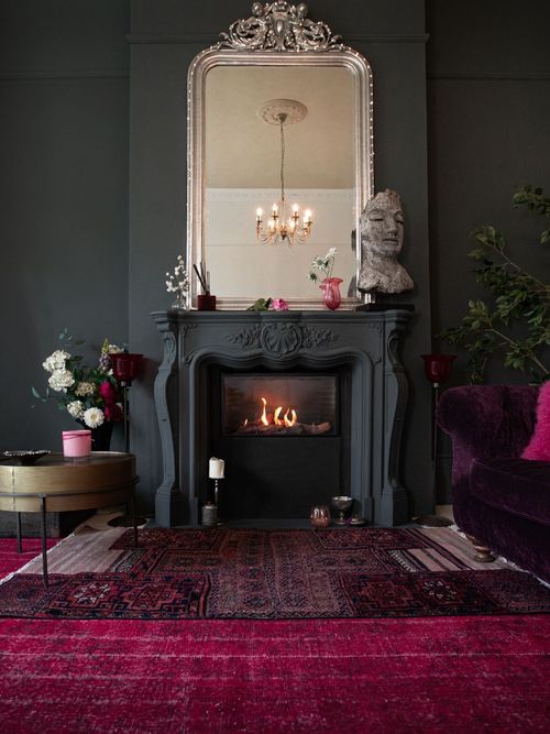 Sujet von einem Wohnzimmer mit schwarzem Kamin, großen Spiegel und Teppich in der Trendfarbe Viva Magenta.