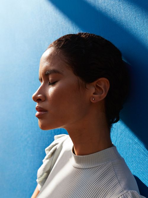 Porträtaufnahme von einer Frau, die bei einer blauen Wand steht und die Sonnenstrahlen genießt.