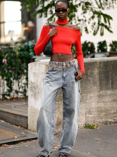 Street Style Look von der Paris Fashion Week, wo ein Model ein Schulterfreies Oberteil mit Baggy Jeans und Hüftgürtel trägt.