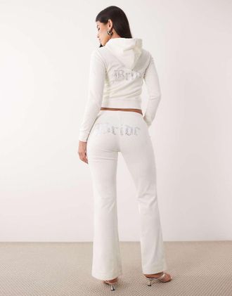 Juicy Couture pantaloni della tuta coordinati in velluto con scritta bride, strass, vita bassa e fondo svasato, color crema-Bianco