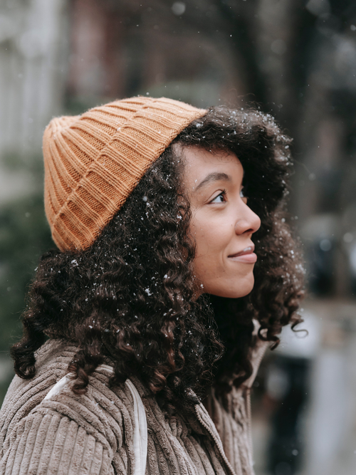 Eine Frau mit Locken, die eine Mütze trägt, während es schneit