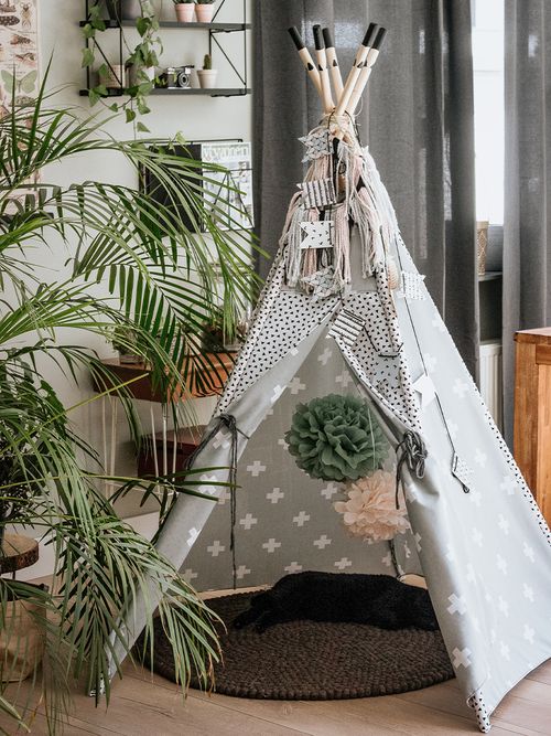 Ein Tipi-Zelt mit Pompons und einem runden Teppich darunter auf dem eine Katze liegt.