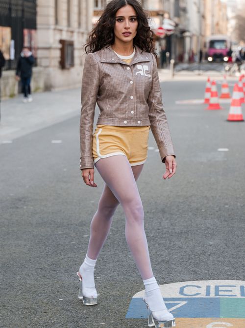 Livia Nunes Marques wears brown checked Courreges jacket, yellow sporty shorts, white tights, white socks, clear platform heels, outside Courreges, during the Womenswear Fall/Winter 2024/2025 as part of Paris Fashion Week on February 28, 2024 in Paris, France.
