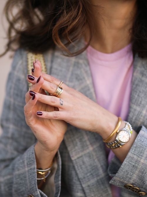 Close up einer Frau mit rosa Pulli unter einem karierten Blazer und rot lackierten Nägeln.