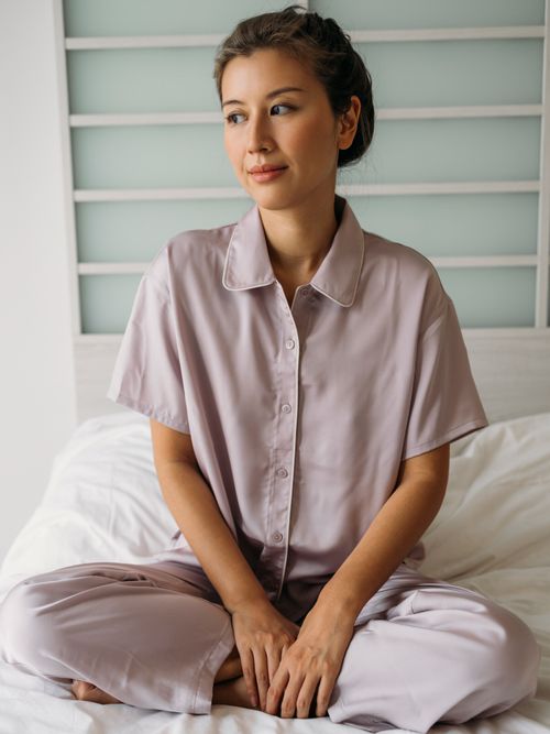 Frau sitzt aufrecht am Bett in einem rosafarbenen Schlafset.