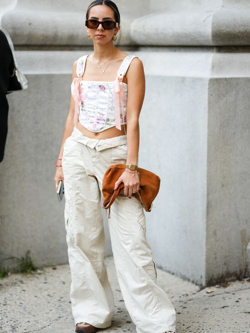 Street Style Look von der New York Fashion Week, wo ein Gast ein geblümtes Korsagen-Crop-Top, Cargohose und Tasche aus Veloursleder trägt.