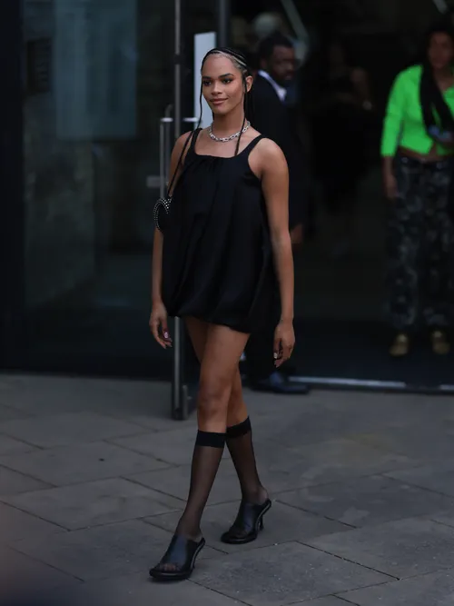 Yasmin Finney was seen wearing black leather high heels, black transparent socks, a black short dress, a Tiffany & Co City Hardwear Diamond silver chain, a black bag with lots of ornaments on it and braids before JW Anderson Fashion Show during London Fashion Week September 2023 at the on September 16, 2023 in London, England.