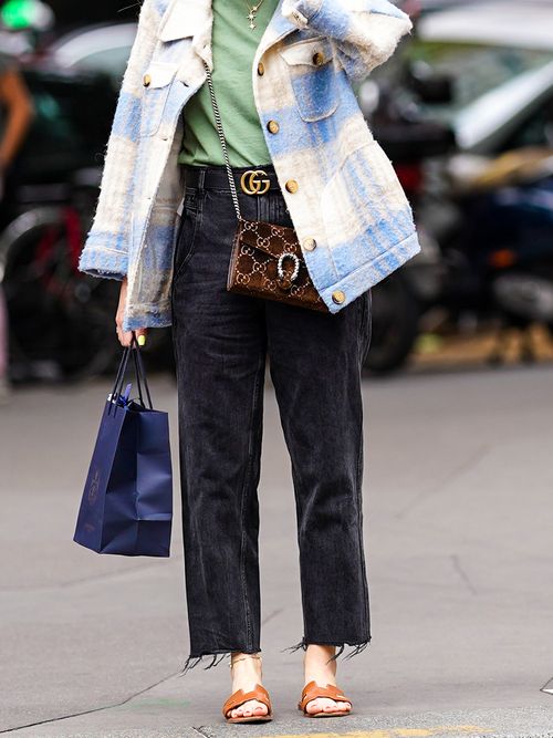 Close-up von einem Streetstyle mit schwarzer Jeans, karierter Jacke, einem grünen T-Shirt und einem Gürtel und einer Tasche von Gucci.