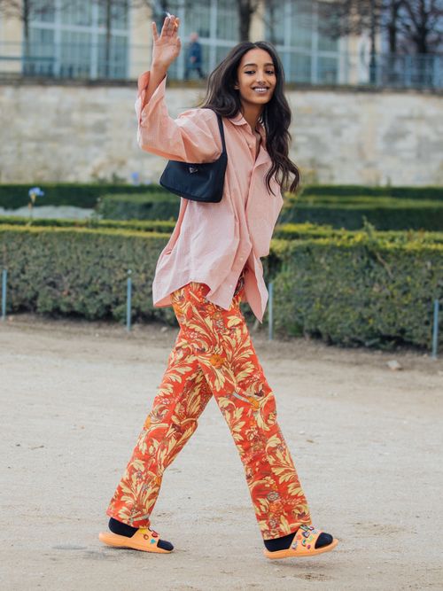 PARIS, FRANCE - FEBRUARY 25: Model Mona Tougaard waves and wears a peach gingham button-up shirt, black Prada mini bag, orange floral print Dries van Noten pants, black socks, and orange chunky embellished sandals after the Dior show during Paris Fashion Week Fall/Winter 2020 on February 25, 2020 in Paris, France. (Photo by Melodie Jeng/Getty Images)
