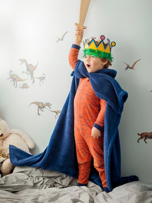 Junge in rotem Schlafanzug mit einem Umhang und einer selbstgebastelten Krone.