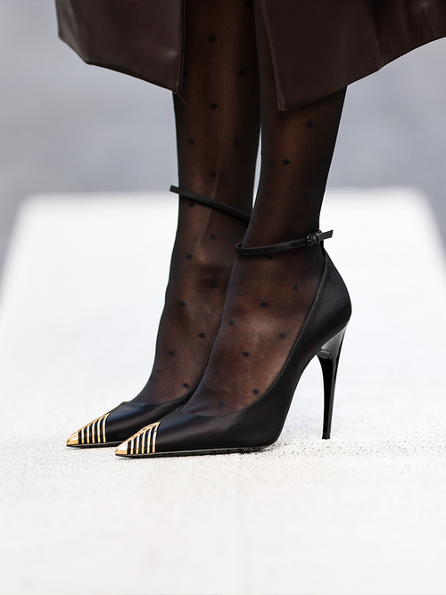 Pumps mit einer goldenen Spitze und einem Knöchelriemen zu gepunkteten Strumpfhosen.