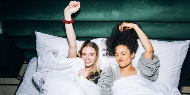 Zwei Frauen, die nebeneinander im Bett liegen und gerade aufwachen.