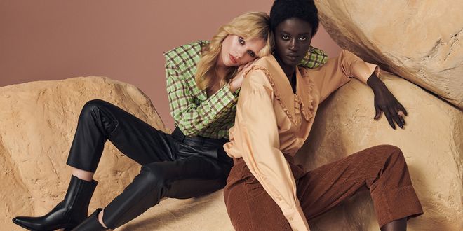 Frau mit Karobluse und Lederhose und eine weitere Frau mit Cordhose und Rüschenbluse.