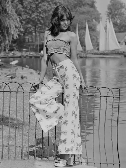Ein Model trägt eine bunten Flared-Hose mit bauchfreiem Top und Plateau-Sandaletten in 1972.
