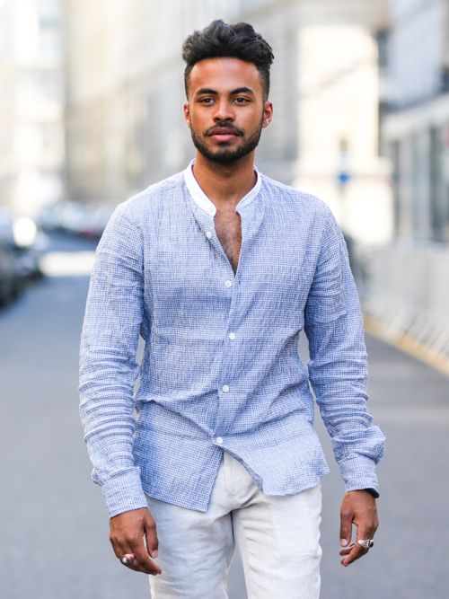 Theo Kimbaloula trägt ein gestreiftes Hemd mit Stehkragen und eine weiße Hose in Paris.