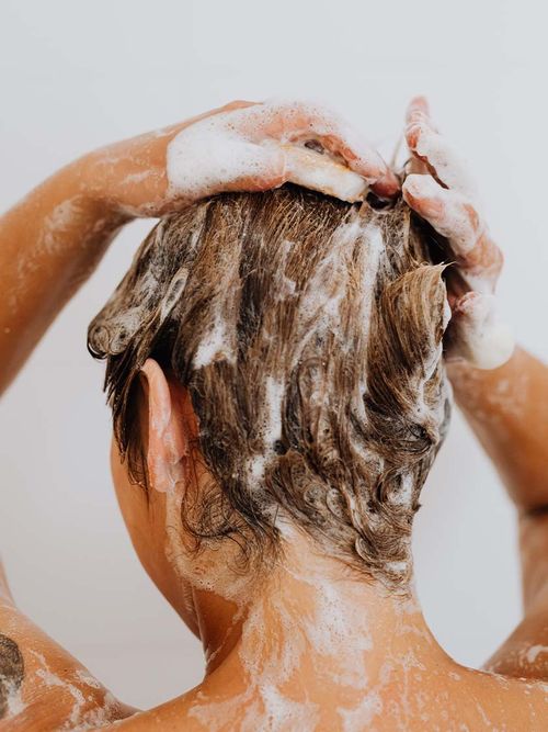 Frau von hinten, die sich gerade die Haare mit Shampoo einschäumt.