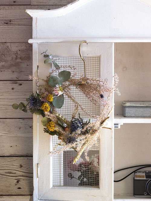 Kranz aus Trockenblumen der an einem weißen Schrank hängt.
