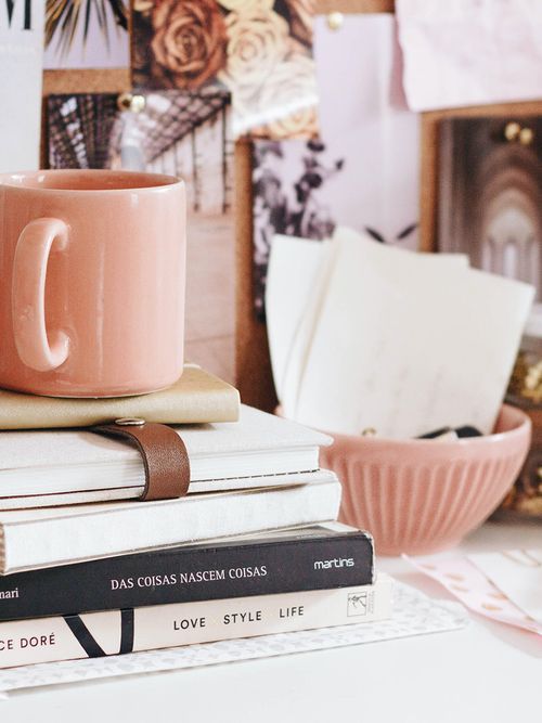 Ein Tisch mit vielen gestapelten Büchern, einer rosa Tasse und Schüssel.