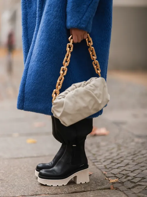 A guest wear a blue coat with a beige bag and a black pair of Copenhagen boots