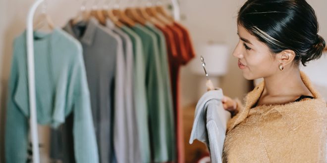 Frau mit beigem Pullover steht vor einer weißen Kleiderstange mit bunten Klamotten.