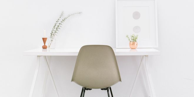 Weißer Schreibtisch vor weißer Wand und ein grauer Eames Stuhl steht davor.