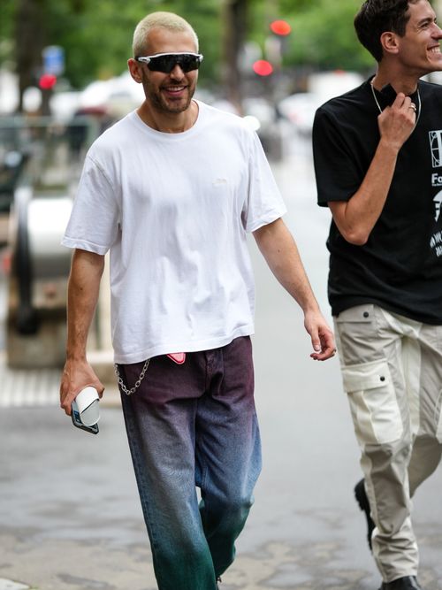 Street Style Look von der Paris Fashion Week, wo ein Gast weißes T-Shirt, mit Baggy-Jeans und sportlicher Sonnenbrille trägt.