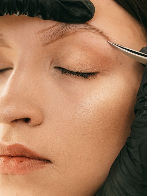 Einer Frau mit angezeichneten Augenbrauen werden gerade die Augenbrauen gezupft.