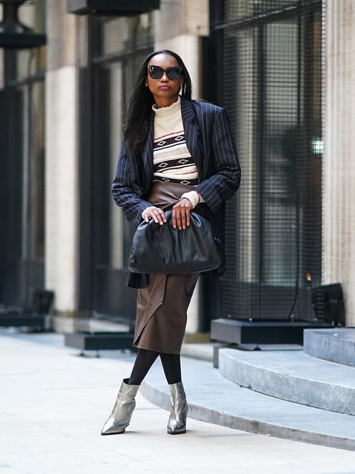 Streetstyle mit einem braunen Lederrock, einem weißen Strickpullover und einem gestreiften Blazer.