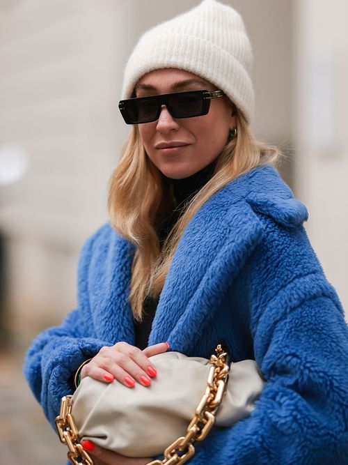 Sonja Lyson mit einem blauen Teddy Coat einer weißen Mütze und einer weißen Bottega Veneta Clutch.