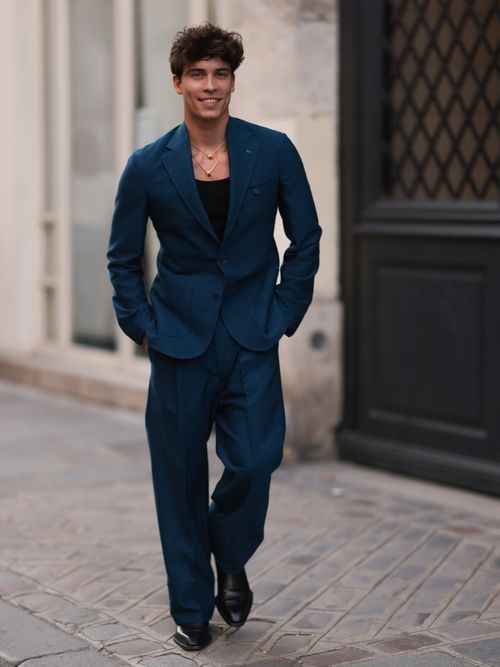 Elevator Boy Tim Schäcker trägt einen blauen Anzug mit schwarzem T-Shirt und Goldketten auf der Paris Fashion Week.